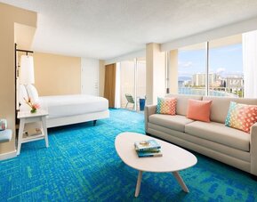 Bright suite with king bed, sofa seating area, colorful pillows, and ocean-facing balcony at The Twin Fin Hotel.