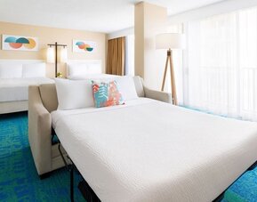 Spacious suite with two beds, sofa bed, and large window with sheer curtains at The Twin Fin Hotel.