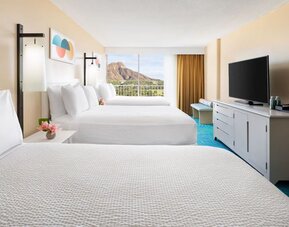 Room with three double beds, TV console, and balcony facing mountain view at The Twin Fin Hotel.