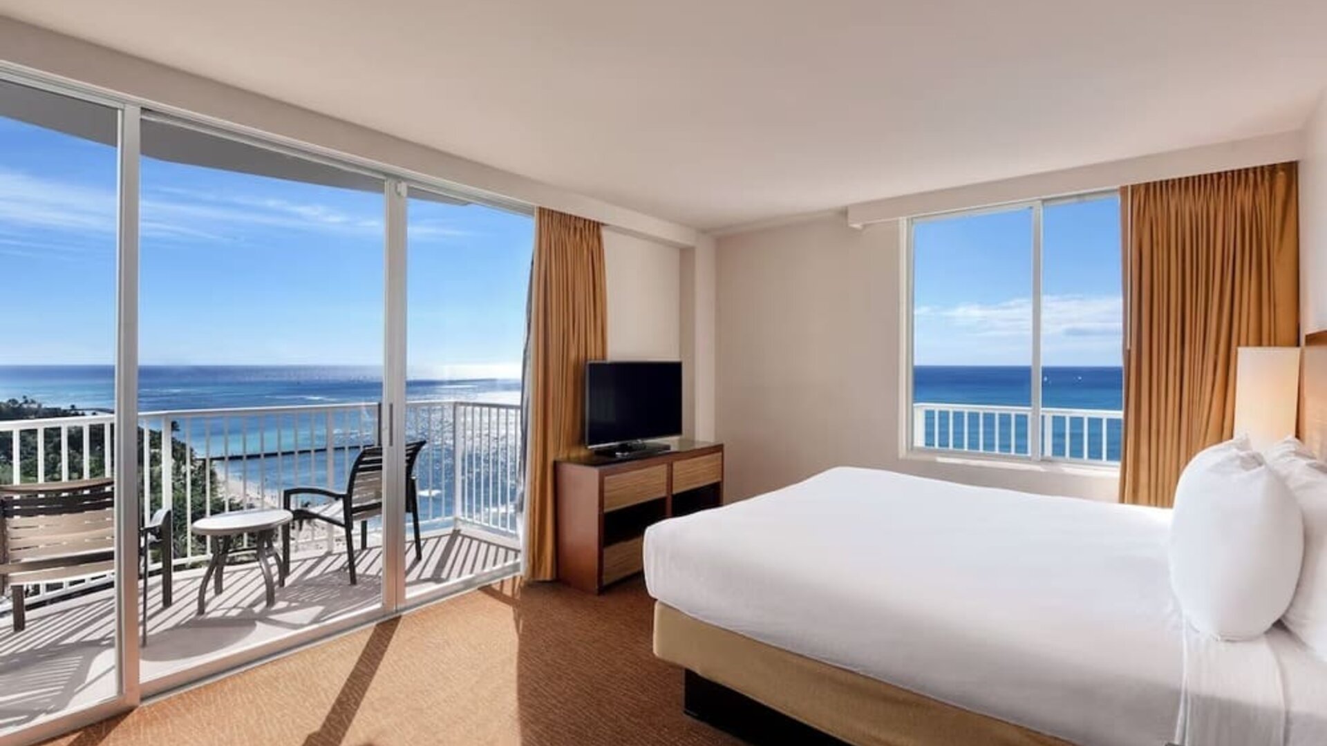 Bright corner room with king bed, large windows, balcony, and sweeping ocean views at Park Shore Waikiki.