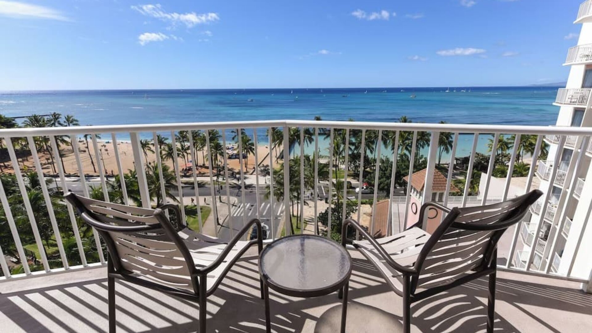 Balcony with two chairs and table overlooking Waikiki Beach, palm trees, and ocean at Park Shore Waikiki.