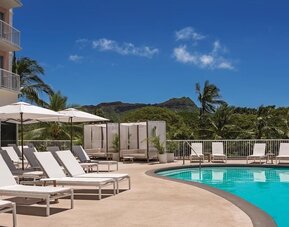 Pool deck with sun loungers, umbrellas, and mountain backdrop at Park Shore Waikiki.