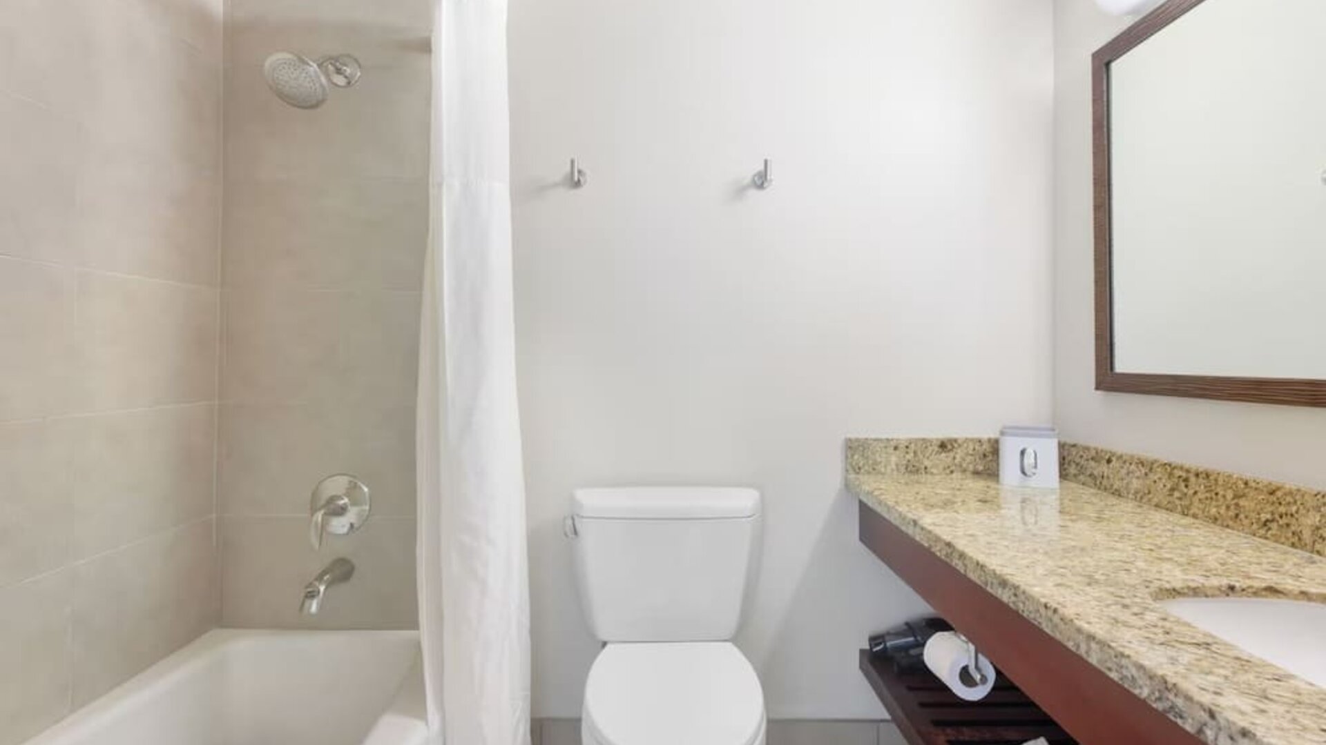 Bathroom with bathtub and shower, granite vanity, mirror, and white tiled walls at Park Shore Waikiki.