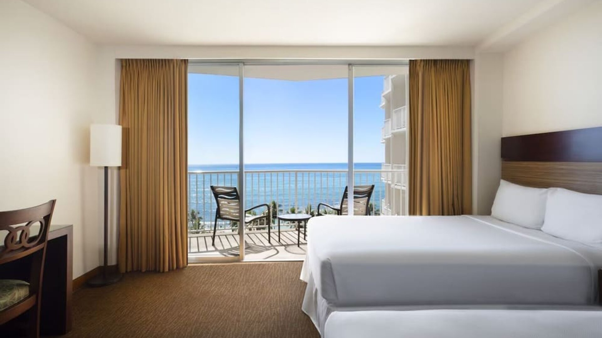 Room with two beds, balcony, and ocean view through sliding glass doors at Park Shore Waikiki.