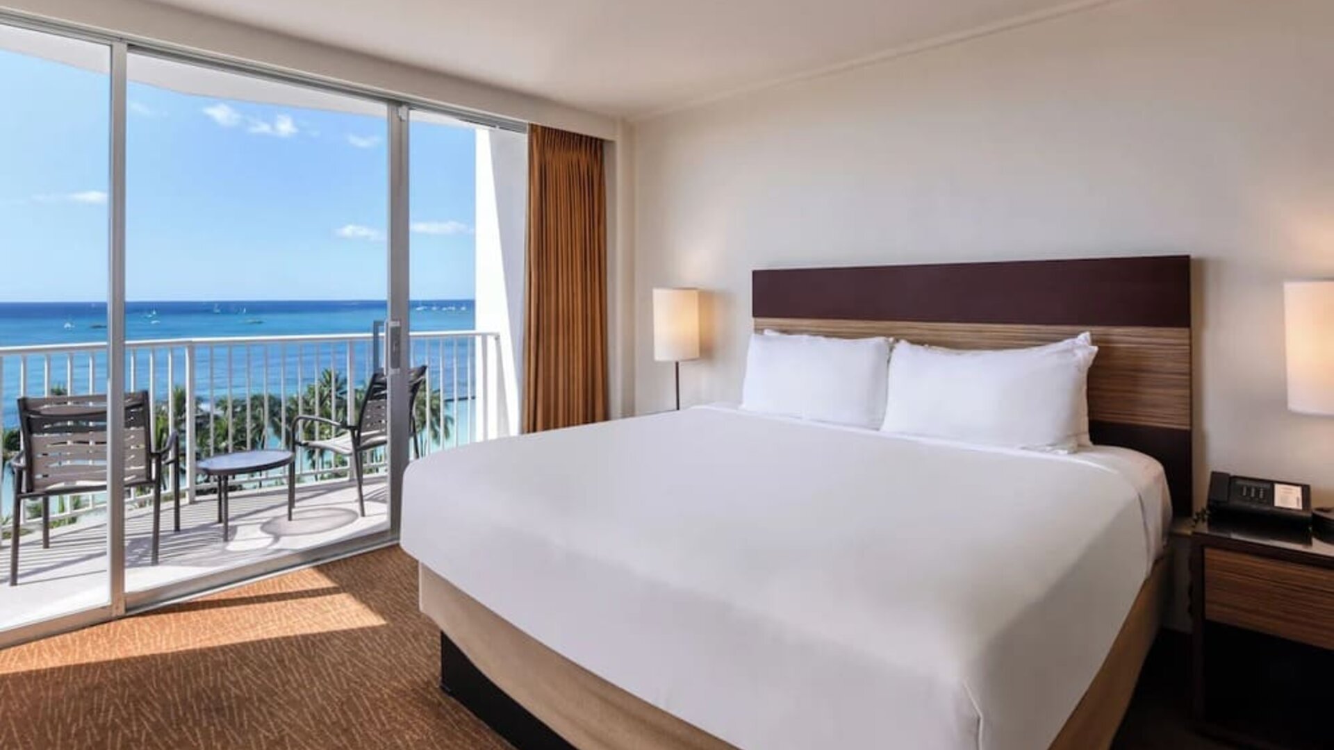 King bed room with ocean-facing balcony, desk, and TV at Park Shore Waikiki.