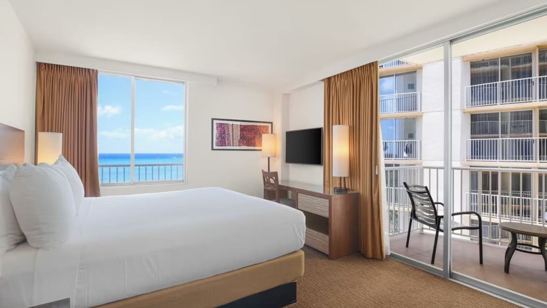 King bed room with balcony view of neighboring buildings and partial ocean view at Park Shore Waikiki.
