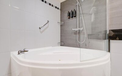 Bathroom with curved bathtub, glass shower screen, and mounted toiletries at Atlantic Tower Hotel Liverpool By Sunday.