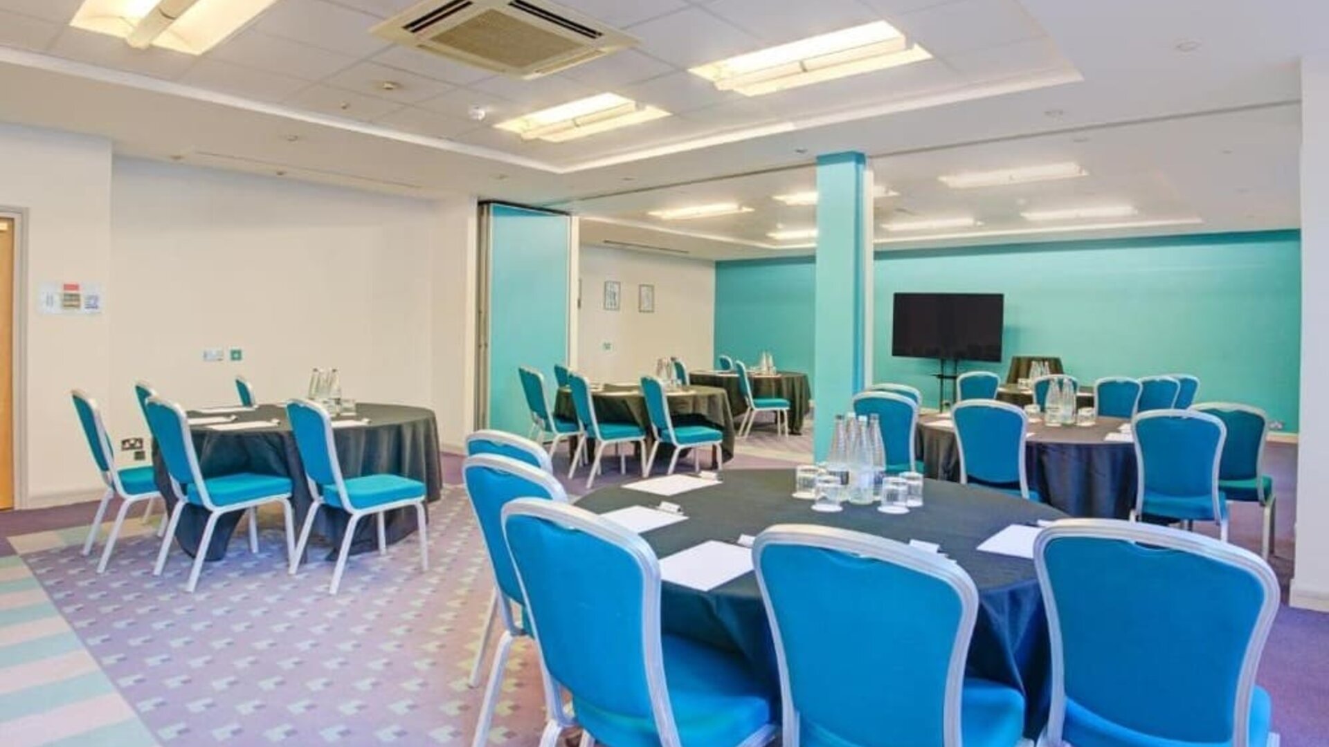 Meeting room with round tables, blue chairs, and presentation screen at Atlantic Tower Hotel Liverpool By Sunday.