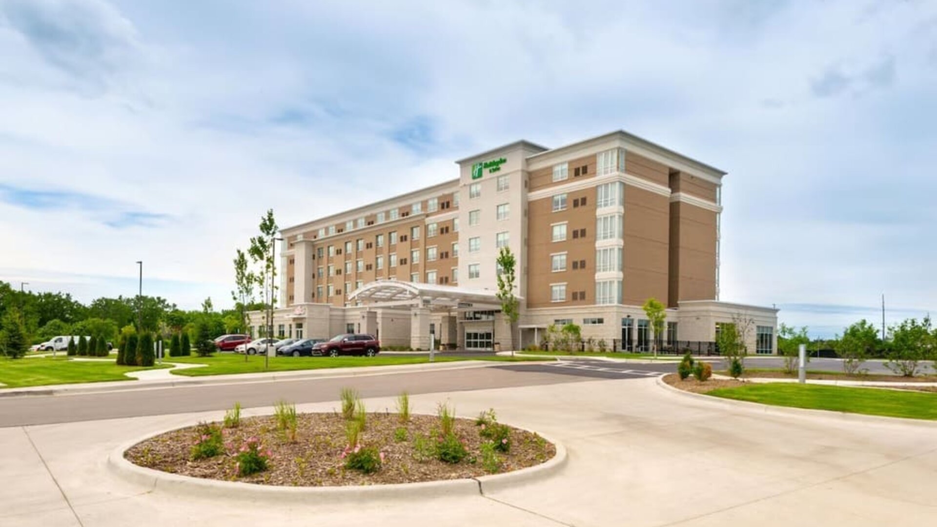 Exterior view of multi-story hotel building with driveway and landscaped entrance at Holiday Inn & Suites Farmington Hills - Detroit NW By IHG.