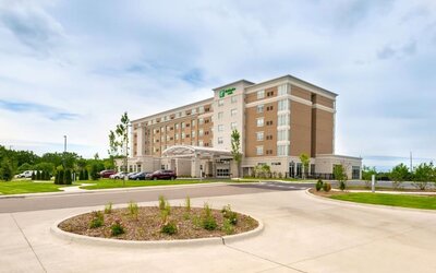 Exterior view of multi-story hotel building with driveway and landscaped entrance at Holiday Inn & Suites Farmington Hills - Detroit NW By IHG.