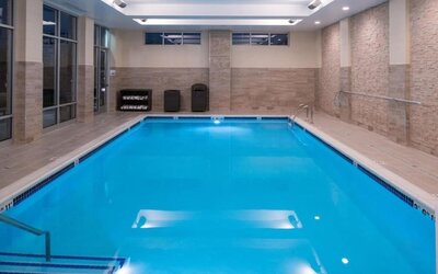 Indoor swimming pool with steps, tiled walls, and ceiling lights at Holiday Inn & Suites Farmington Hills - Detroit NW By IHG.