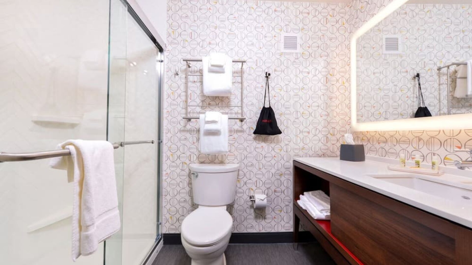 Bathroom with walk-in shower, toilet, towels, and illuminated mirror at Holiday Inn & Suites Farmington Hills - Detroit NW By IHG.