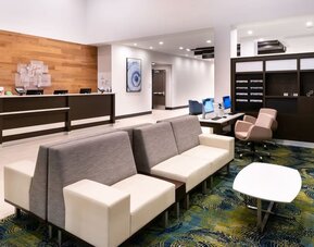 Lobby with front desk, seating area, patterned carpet, and modern decor at Holiday Inn & Suites Farmington Hills - Detroit NW By IHG.