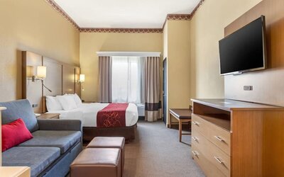 Guest room with king bed, sofa seating, ottoman, dresser, and wall-mounted TV at Comfort Suites Bush Intercontinental Airport.