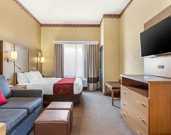 Guest room with king bed, sofa seating, ottoman, dresser, and wall-mounted TV at Comfort Suites Bush Intercontinental Airport.