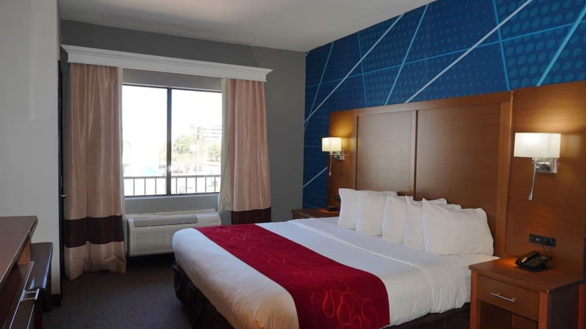 Day room with accent wall, bedside lighting, and window with curtains and air conditioning unit at Comfort Suites Bush Intercontinental Airport.