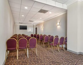 Meeting room with rows of chairs, wall-mounted TV, and whiteboard in a compact space at Comfort Suites Bush Intercontinental Airport.