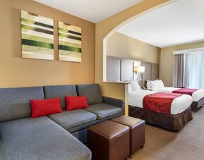 Suite with two beds, sofa seating area, ottomans, and decorative wall art at Comfort Suites Bush Intercontinental Airport.