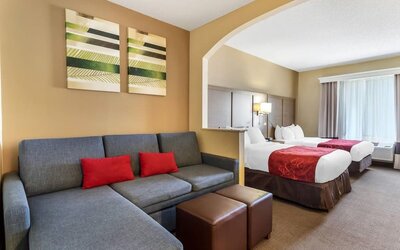 Suite with two beds, sofa seating area, ottomans, and decorative wall art at Comfort Suites Bush Intercontinental Airport.