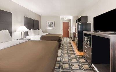 Room with two beds, dresser, TV, microwave, mini fridge, and patterned flooring at Suburban Studios Mason Hwy-42.