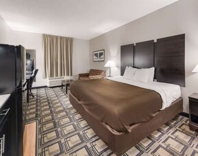 King room with large bed, bedside tables, lamps, and seating area with armchair and table at Suburban Studios Mason Hwy-42.