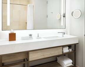 Modern bathroom with large mirror, vanity sink, mounted magnifying mirror, and neatly arranged towels at M Social New York Downtown.