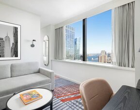 Lounge area with sofa seating, floor lamp, wall art, and large window overlooking city buildings at M Social New York Downtown.