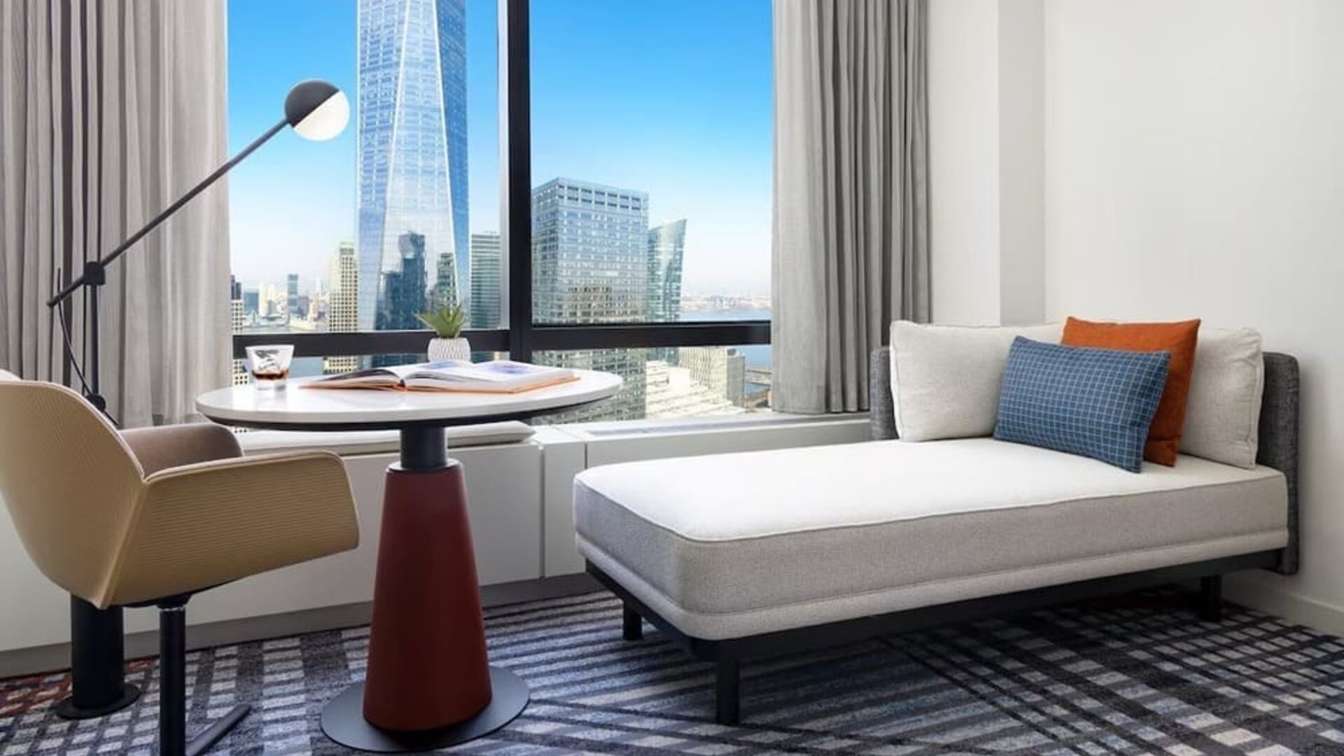 Seating area with chaise lounge, table, and floor-to-ceiling window showcasing city views at M Social New York Downtown.