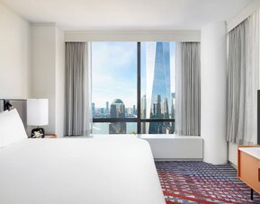 Guest room with king bed, large window, and city skyline view at M Social New York Downtown.