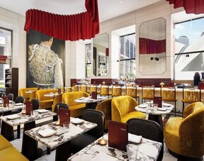 Restaurant dining area with marble tables, red accents, gold seating, and statement artwork at M Social New York Downtown.