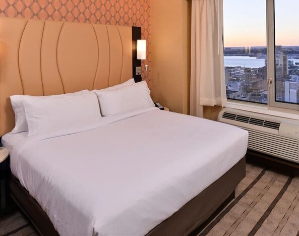 Guest room with king bed and large window allowing natural light and city views at Holiday Inn New York City - Times Square By IHG.