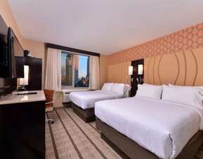 Guest room with two double beds, modern furnishings, and city view window at Holiday Inn New York City - Times Square By IHG.