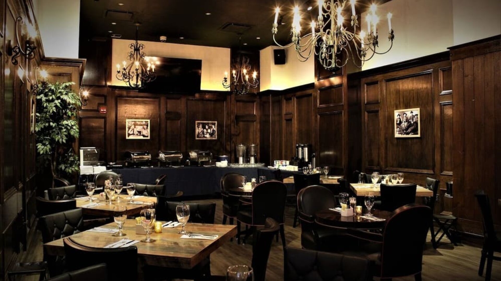 Restaurant dining area with wooden tables, chandeliers, and warm ambient lighting at Holiday Inn New York City - Times Square By IHG.