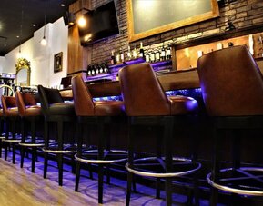 Bar area with high stools, wooden finishes, and illuminated shelving at Holiday Inn New York City - Times Square By IHG.