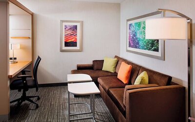 Guest suite with sofa seating area, workspace desk, and modern décor at Springhill Suites Carle Place.