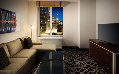 Living area with sofa, coffee table, television, and city view through window at Hilton Brooklyn New York.