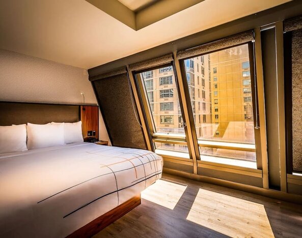 Guest room with king bed and large angled windows providing natural light and city views at La Quinta Times Square South.