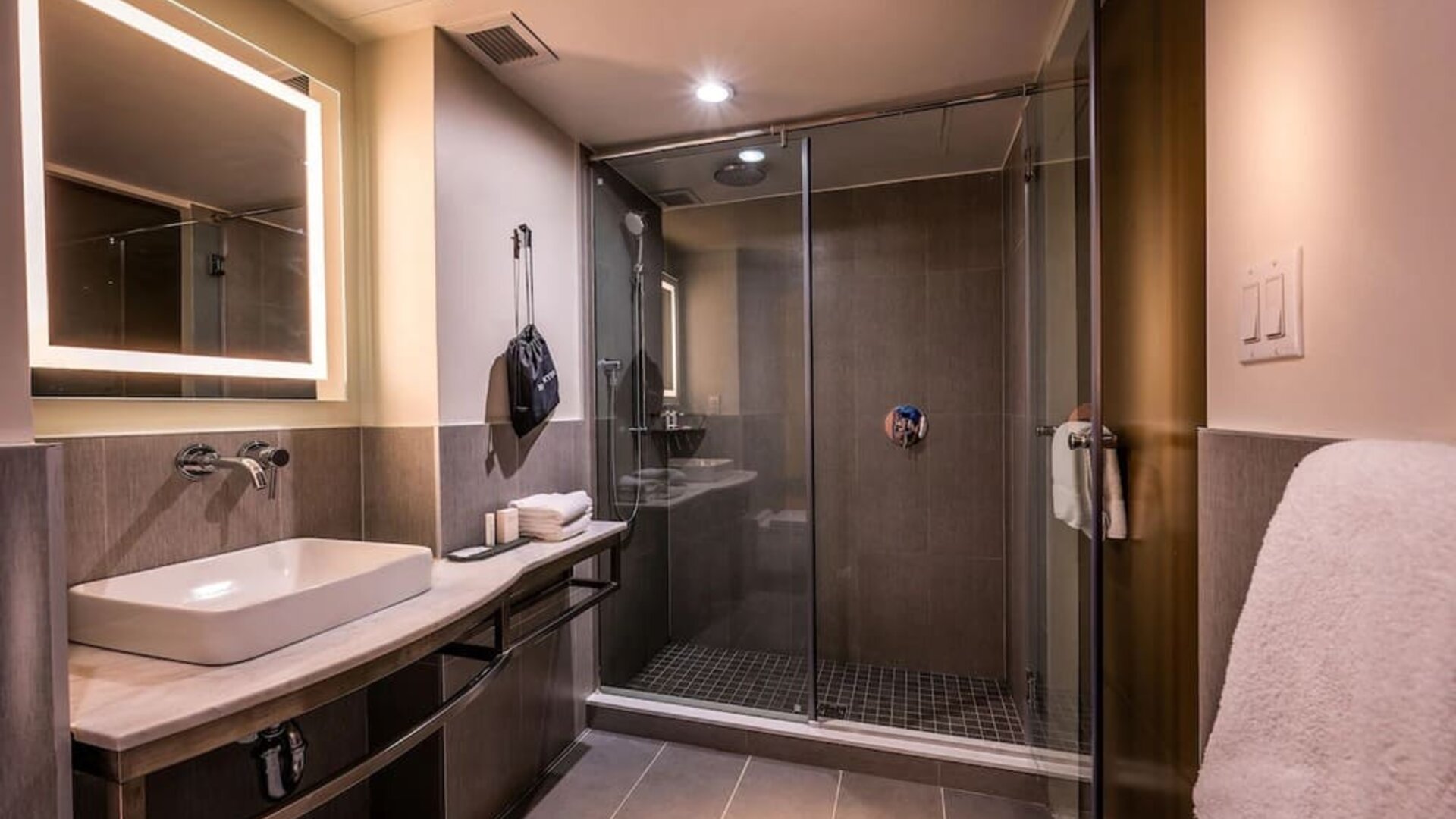 Bathroom with walk-in glass shower, sink, illuminated mirror, and modern finishes at La Quinta Times Square South.