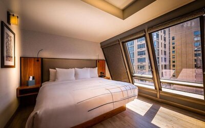 Guest room with king bed and angled floor-to-ceiling windows offering city views at La Quinta Times Square South.