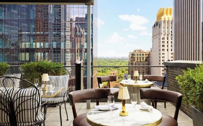 Rooftop terrace with seating, dining tables, and views of Central Park and city skyline at Le Méridien New York, Central Park.