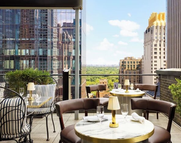 Rooftop terrace with seating, dining tables, and views of Central Park and city skyline at Le Méridien New York, Central Park.
