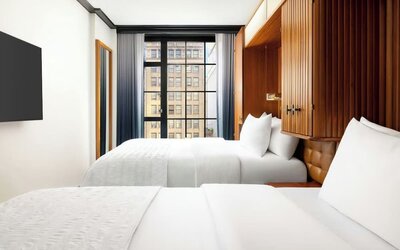Guest room with two beds, wood-paneled headboard, and large window with city views at Le Méridien New York, Central Park.