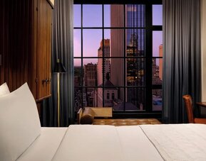 Guest room with king bed and large window showcasing city skyline views at Le Méridien New York, Central Park.