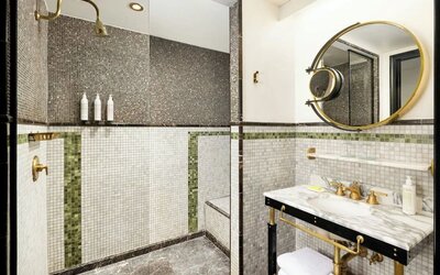 Bathroom with walk-in shower, mosaic tile walls, marble sink, and gold fixtures at Le Méridien New York, Central Park.