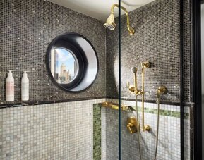 Bathroom with walk-in shower, mosaic tiles, and gold fixtures at Le Méridien New York, Central Park.