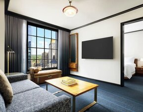 Living area with sofa, coffee table, and connected bedroom space at Le Méridien New York, Central Park.