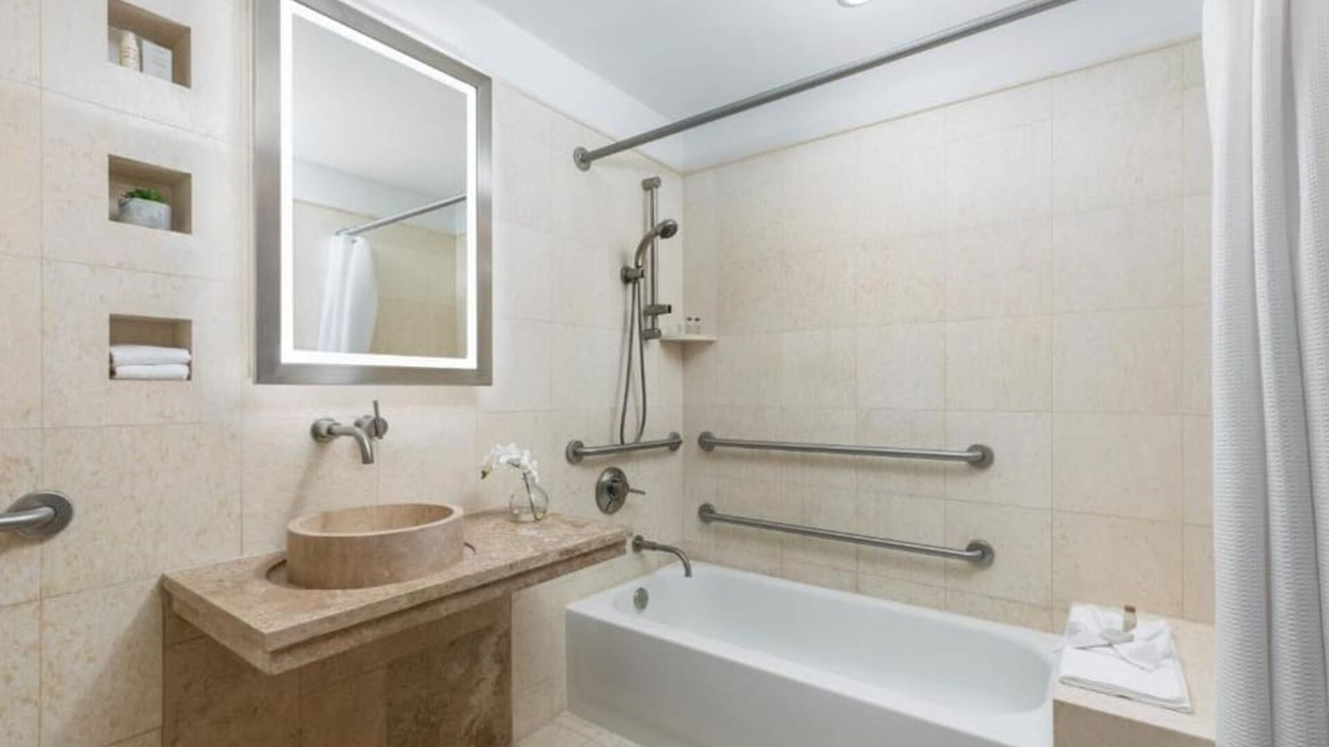 Accessible bathroom with bathtub, grab rails, and stone finishes at Hotel 57.