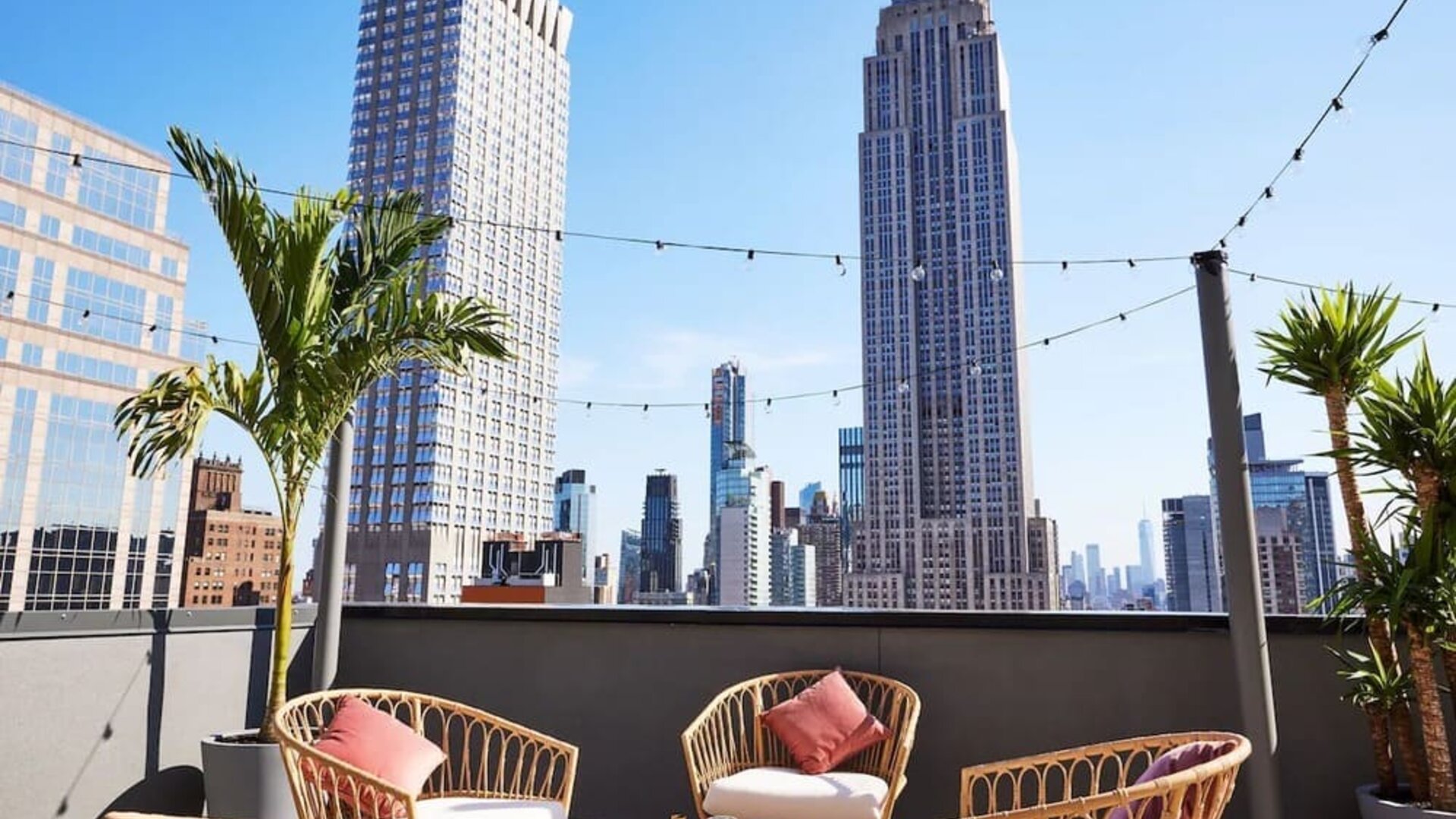 Rooftop terrace with seating, string lights, and skyline views including the Empire State Building at Hotel Hendricks.