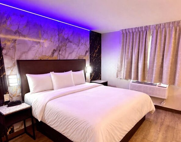 Modern guest room with king bed, marble feature wall, ambient LED lighting, and window with curtains at Imperial Hotel.