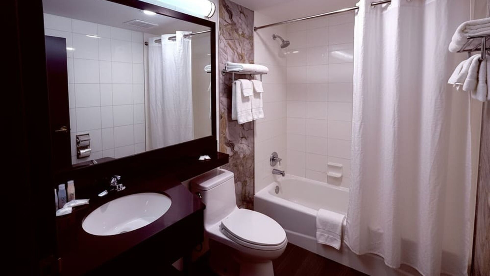 Bathroom with bathtub, shower, large mirror vanity, and neatly arranged towels at Imperial Hotel.